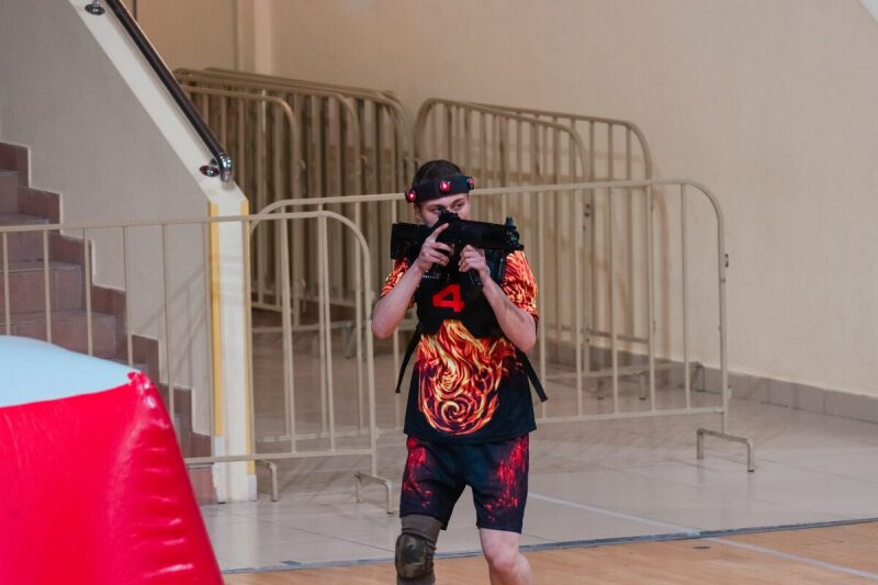 Боец LASERWAR в яркой футболке целится из автомата.
